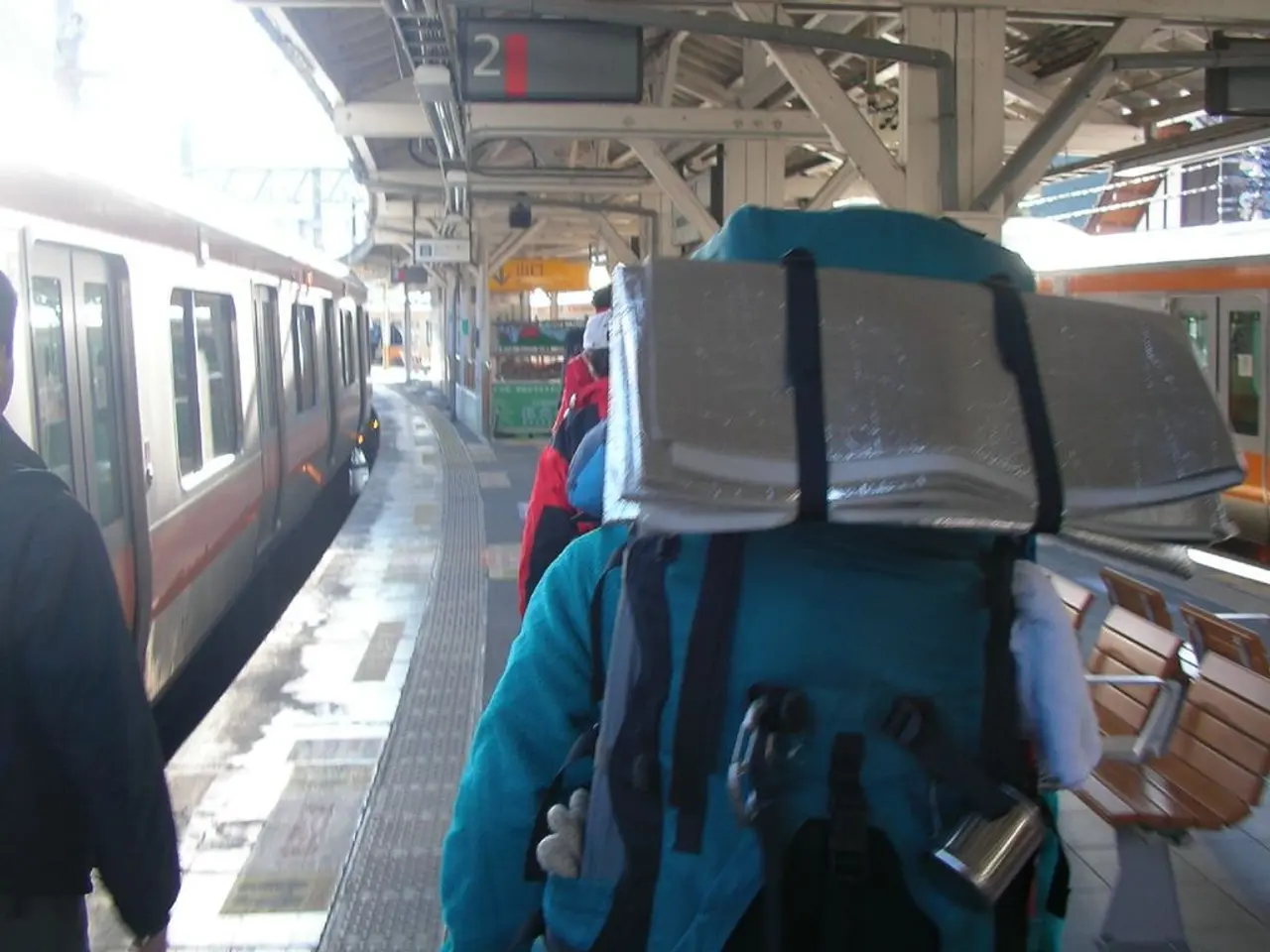In this image, we can see a railway station. There are persons beside the train. There is a stall...