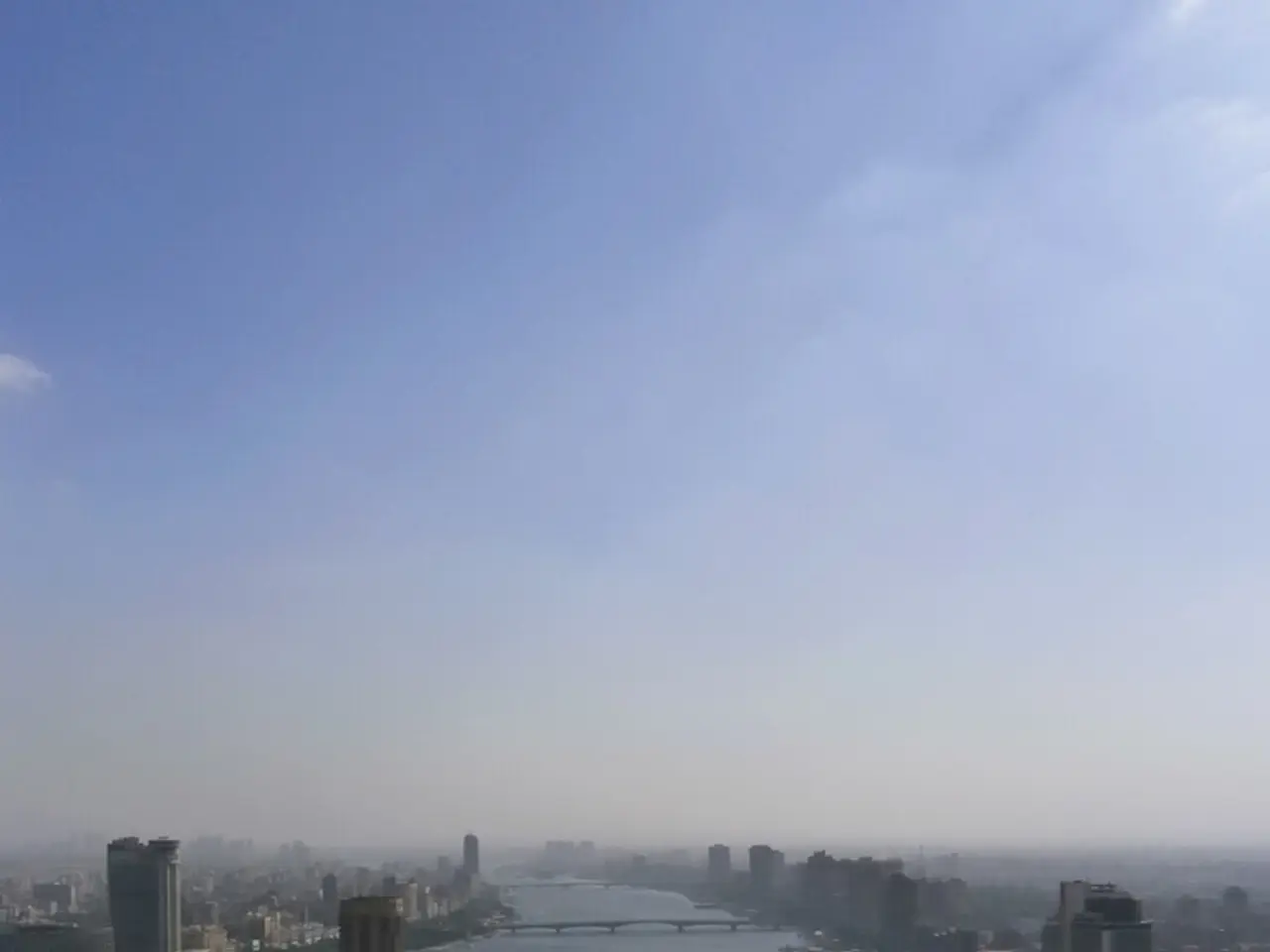 In this image we can see buildings, road, vehicles, poles, trees, water, bridge and sky.