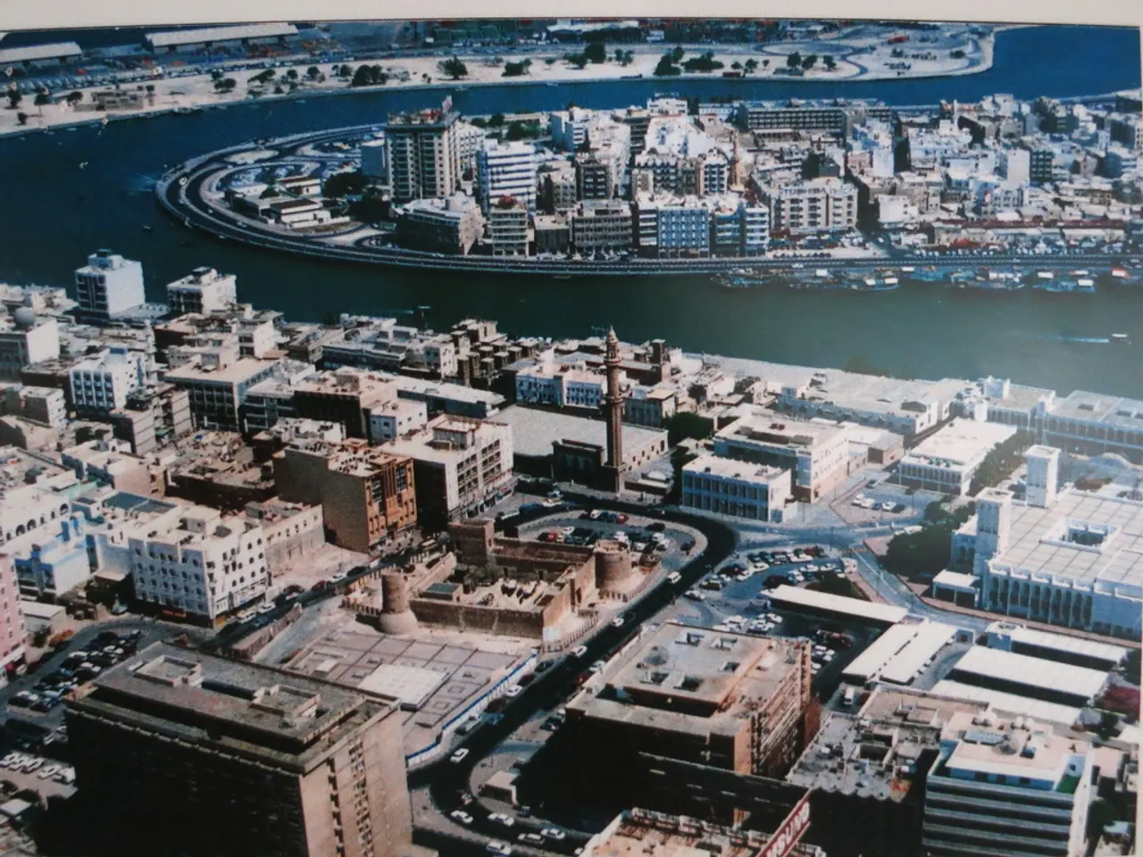 In this image there are buildings, roads cars and there is a sea, in the middle of the sea there...