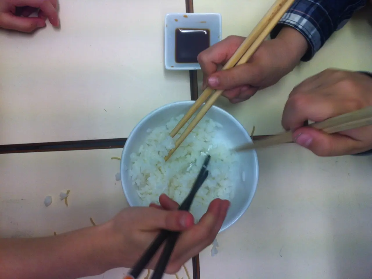 In the image we can see there is a bowl in which there is a rice and people are holding chopsticks...