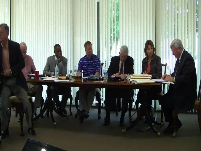 In the image there is a table and there are some papers,bottles on the table in front of the table...