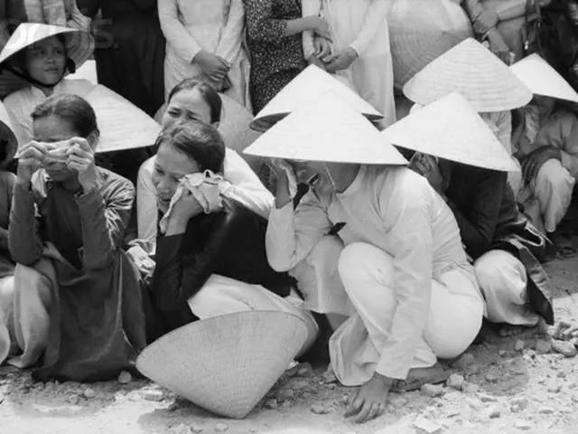 It is the black and white image in which there are few people sitting on the ground by wearing the...